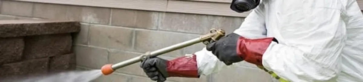 Pest control technician applying exterior insect treatment along a home foundation in Lakeland, FL