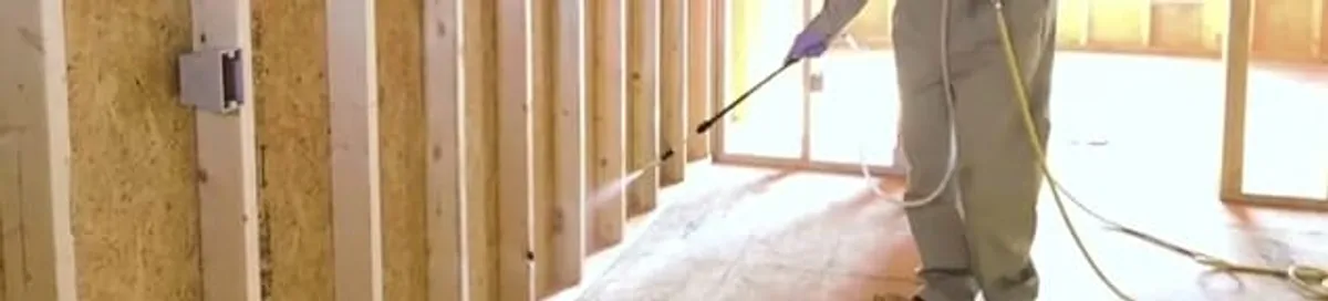 Termite treatment technician applying spray along framing and unfinished walls in Lakeland, FL